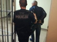 Zdjęcie kolorowe:  zatrzymany mężczyzna prowadzony przez  policjanta.