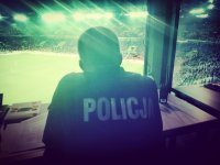 Zdjęcie kolorowe: policjant na stanowisku dowiedzenia obserwuje mecz piłki nożne