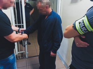Policjant zakłada kajdanki zespolone zatrzymanemu mężczyźnie