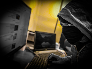 Na zdjęciu zamaskowana postać przed komputerem